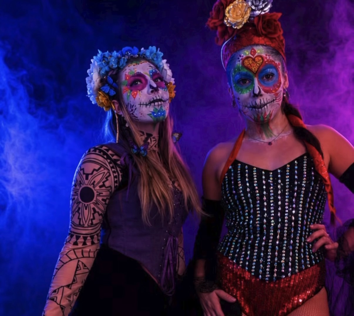 Two sugar skull performers side by side in blue and purple smoke